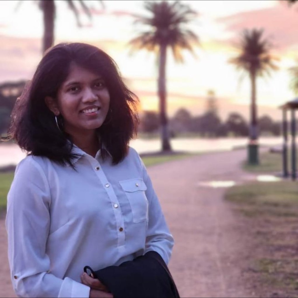 Professional portrait of Gayathri Muthalagu smiling outdoors at sunset with palm trees in the background.